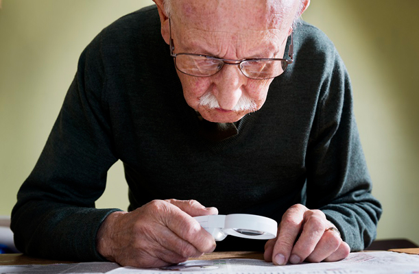 An elderly man reading with a magnifying glass