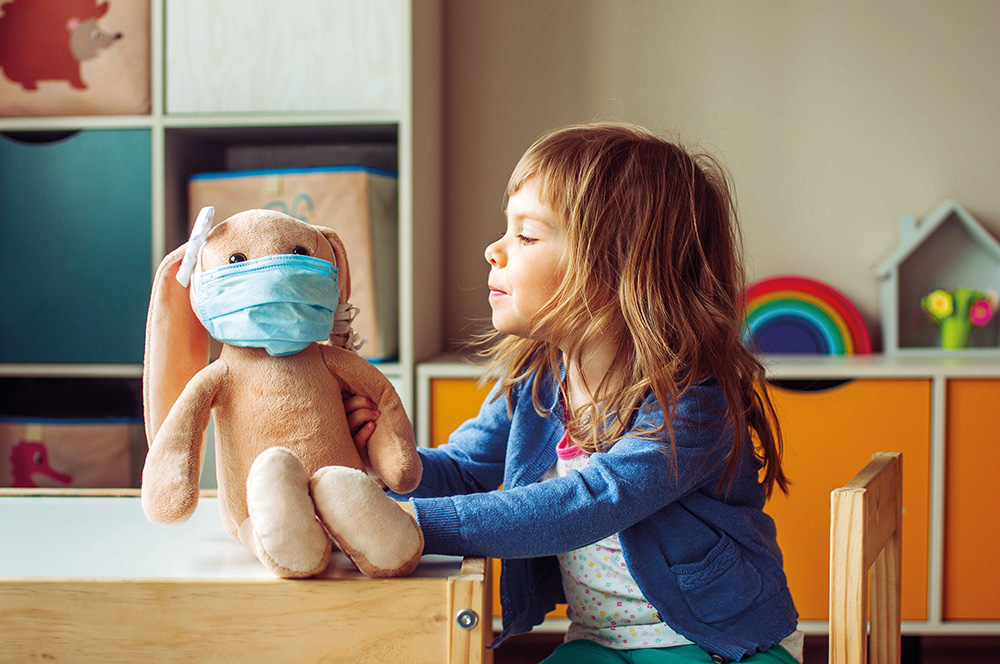 A primary school child playing with a masked teddy bear in a classroom