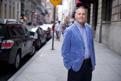 Joel in a blue jacket on a street with lots of cars parked on the side