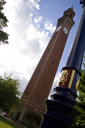 Old Joe clock tower in the sun with a pole on campus in view with the crest painted on it
