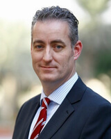 Ben Bailey wearing a black jacket and red and white striped tie