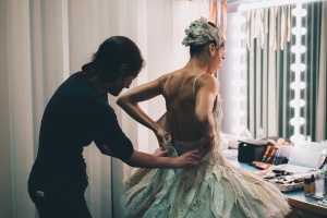 A ballerina getting dressed with the help of a second person