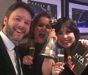 group of three, the person in the middle holding up an award