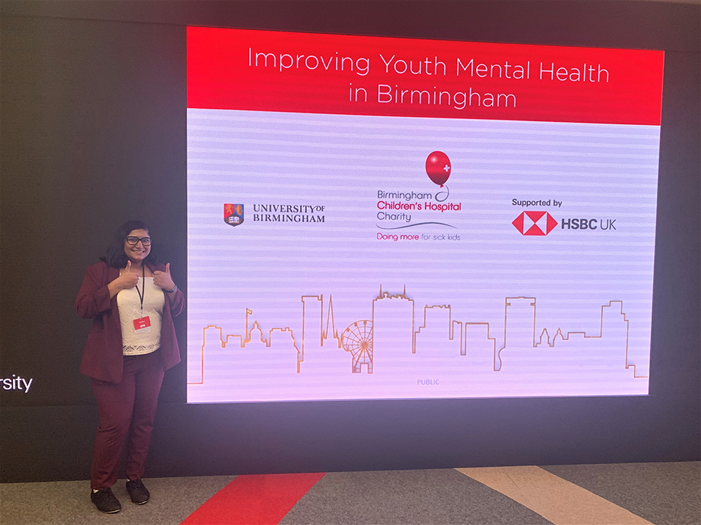 Student stands in front of a sign with University of Birmingham, HSBC and BCH logos on it