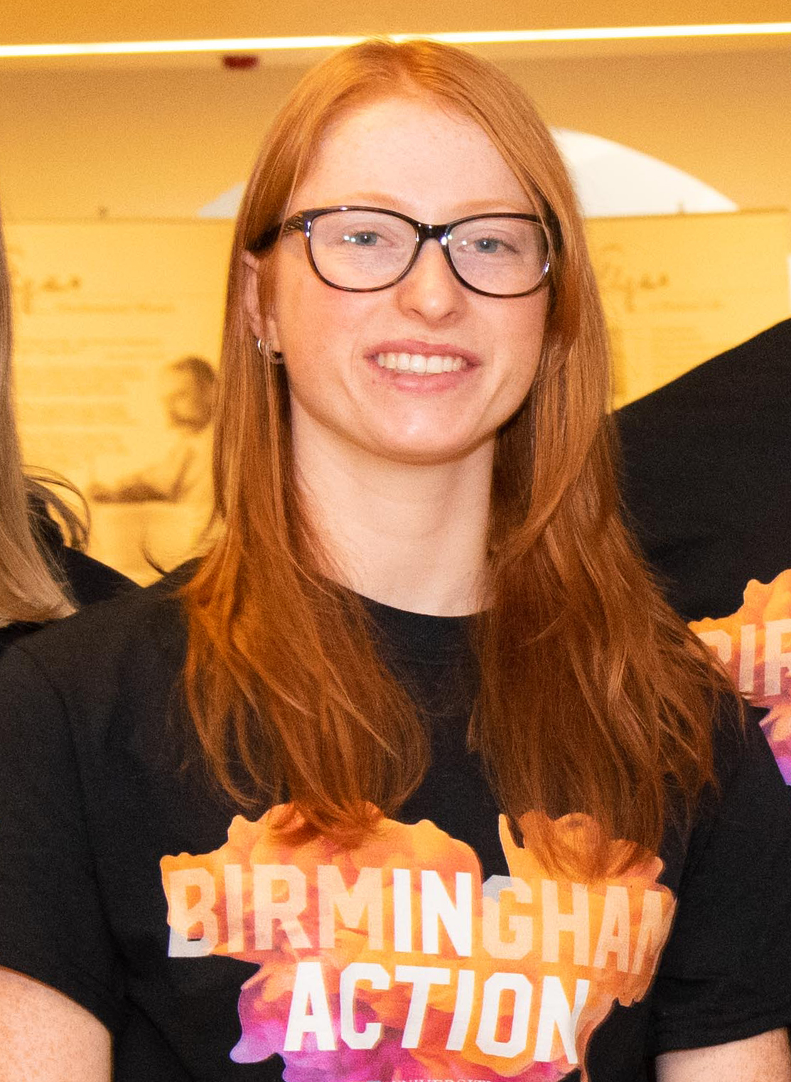 Female student with glasses wearing black and orange t-shirt that says 'Birmingham In Action' 