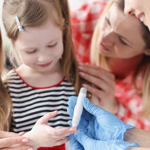 A young girl is helped to take a fingerprick test