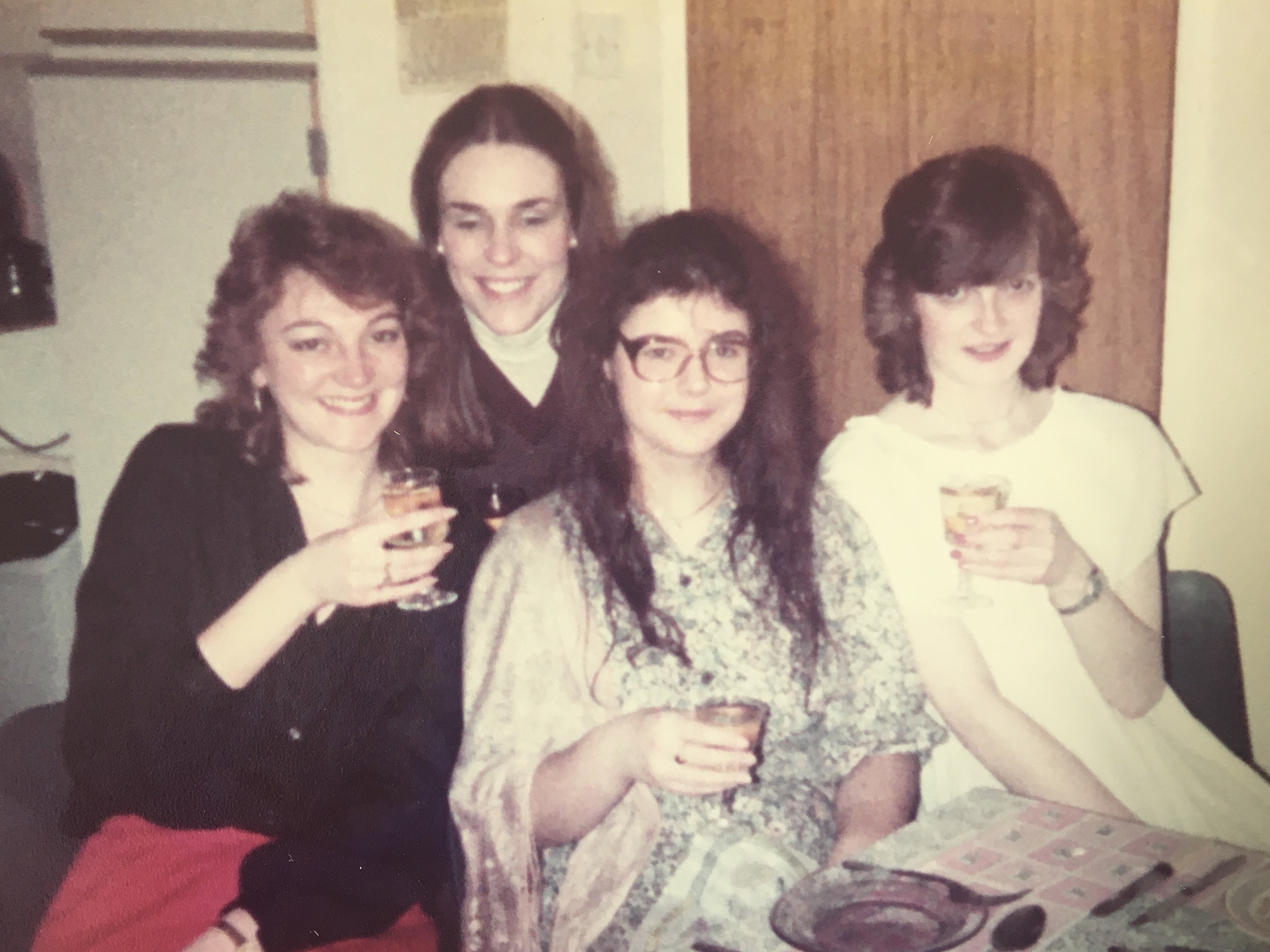 Four friends holding drinks together in the 80's