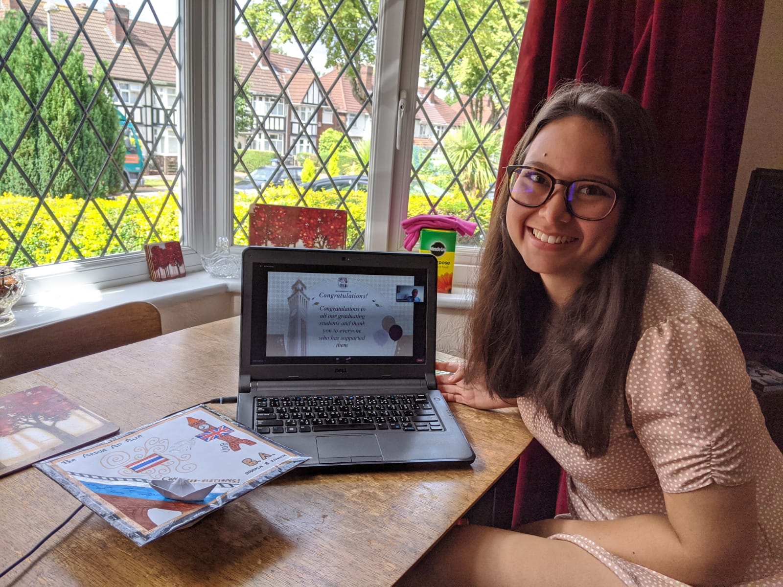 Girl sitting next to laptop with homemade graduation cap next to a window