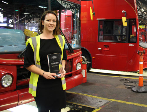 Woman in high visibility jacket holding glass trophy, standing in front of red buses