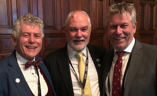 Three men smiling together in front of wood panelling